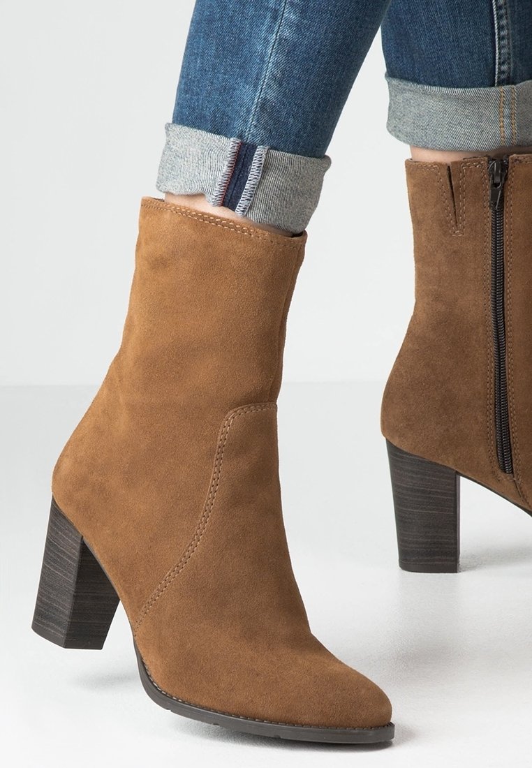 Bottine en daim marron avec un bout pointu et un talon empilé. Dispose d'une fermeture éclair latérale et d'un design sans coutures pour une silhouette lisse.
