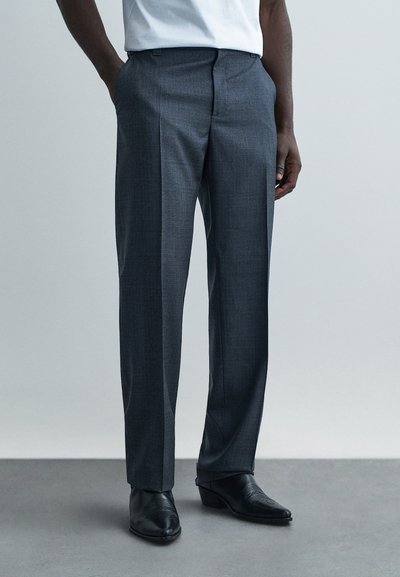 Pantalon gris sur mesure avec une finition texturée, devant plat, deux poches latérales, porté avec des chaussures habillées en cuir noir.