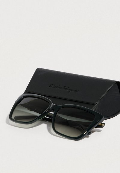 Zielone, duże okulary przeciwsłoneczne z gradientowymi soczewkami, wraz z czarnym, teksturowanym etui z wytłoczonym logo.