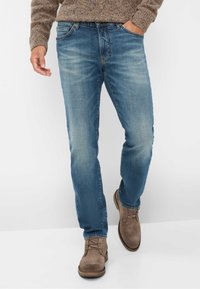 Blauwe denim jeans, rechte pasvorm, met vervagingdetails, vijf zakken en bruine leren laarzen. De textuur lijkt zacht en duurzaam.
