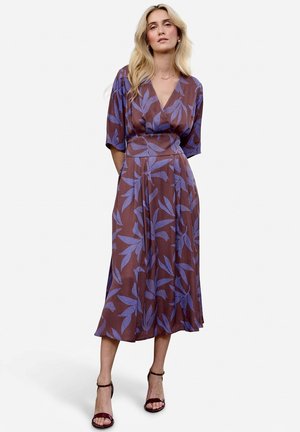 Brązowa sukienka długości do połowy łydki z dużymi niebieskimi wzorami liści, o fasonie kopertowym, z krótkimi rękawami i zwiewnym materiałem. Do tego paseczkowe bordo sandały.