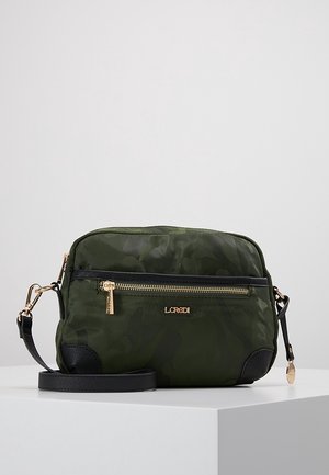 Bolso pequeño de bandolera verde oscuro con patrón de camuflaje, cremallera dorada, borde negro y correa negra ajustable sobre pedestal blanco.