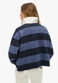 Suéter de algodón con cuello blanco, con rayas horizontales en azul marino oscuro y azul claro. Corte holgado, diseño corto y mangas largas.