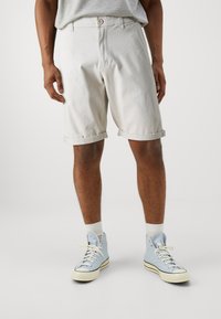 Pantalones cortos de mezclilla blanca con puños enrollados, que cuentan con una bragueta de botones y bolsillos laterales, combinados con zapatillas altas azul claro y calcetines blancos.