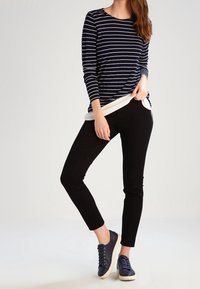 Marinblå och vit randig långärmad topp över en vit skjorta, tillsammans med svarta slim-fit byxor och mörka sneakers med vita sulor.