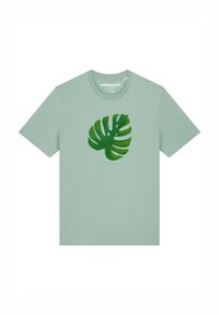 T-shirt en coton vert clair avec un grand motif de feuille de monstera verte au centre. Encolure ronde et manches courtes.