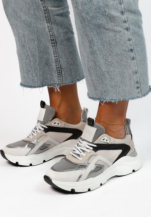 Chunky sneakers with mesh and synthetic textures, featuring a mix of gray, black, and white. Laces and a padded collar for comfort.