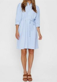Abito camicia a quadri blu chiaro con vita stretta e dettaglio di cravatta. Presenta maniche a tre quarti e una vestibilità comoda, abbinato a sandali scivolati marroni.