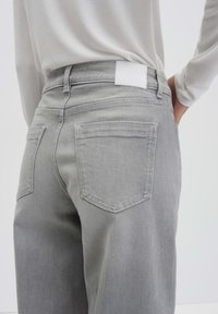 Gray denim jeans with a smooth texture, featuring a white leather patch at the waistband and two back pockets with stitched detailing.