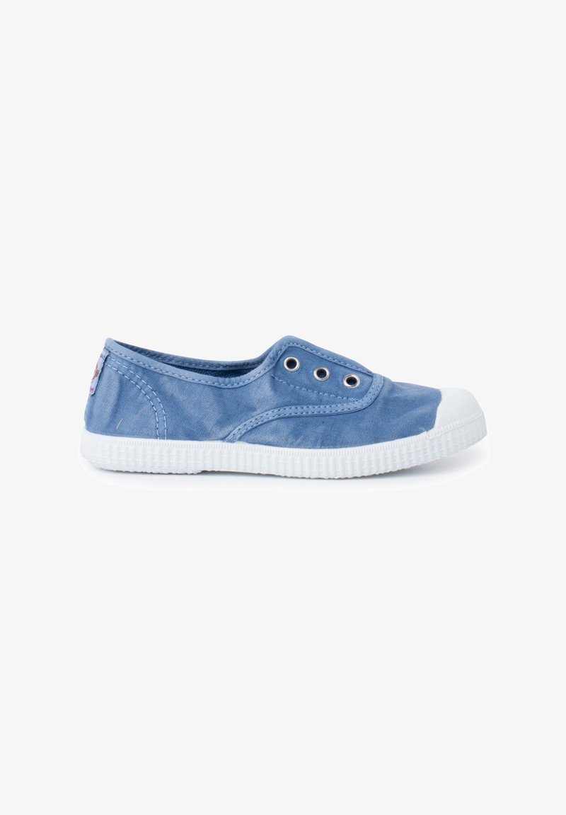 Zapatilla de lona azul tipo slip-on con puntera y suela de goma blanca. Presenta dos ojales de metal para ventilación y un diseño de tela texturizada.