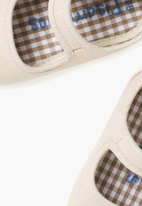 Beżowe płócienne buty slip-on z wycięciami, z brązowo-białym w kratkę podszewką i niebieskim logo na wkładce.