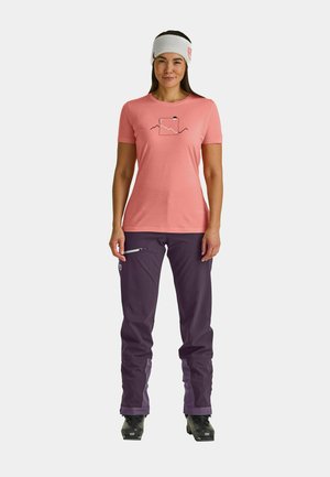 Light pink short-sleeve t-shirt with a mountain graphic, paired with dark purple waterproof pants and black ski boots. White headband accent.