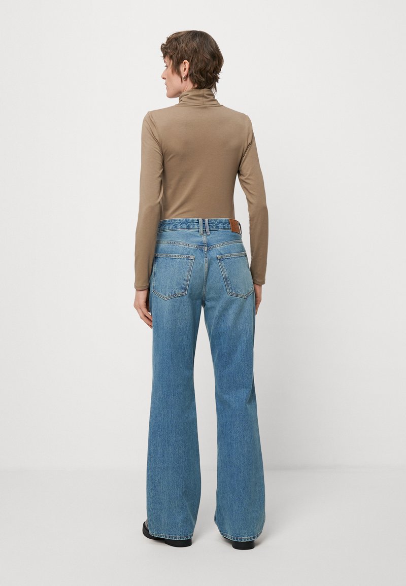 Top marrón de mangas largas y vaqueros acampanados azules con parches traseros, que cuentan con dos bolsillos traseros y una textura de denim ligeramente desgastada.