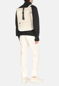 Zaino a rotolo in beige chiaro, caratterizzato da una finitura lucida e elegante, accessori neri e spallacci regolabili. Include una tasca posteriore con zip.