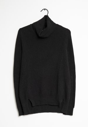 Maglione nero a collo alto a coste, con un taglio loose, caratterizzato da spacco laterale all'orlo e un tessuto morbido e testurizzato. Appeso a un gancio nero.