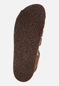 Braune Sandalensohle mit einer strukturierten, griffigen Oberfläche. Abgerundete Form, hergestellt aus strapazierfähigem Material mit einem natürlichen, matten Finish. Leichtes Design.