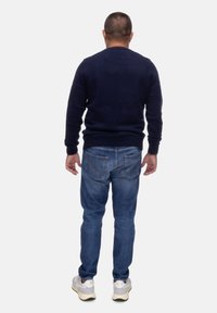 Maglione a maglia blu navy, aderente in vita, abbinato a jeans azzurri con cuciture a contrasto. Indossato con sneakers bianche e grigie.