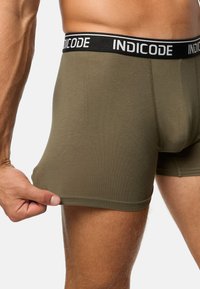 Olívazöld boxer alsónadrág, puha anyagból készült, fekete elasztikus derékpánttal, fehér betűkkel "INDICODE" felirattal.