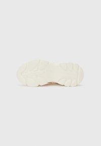 Sål av sko med teksturert gummi i off-white, med sikksakk-mønstre og en subtil merkevarelogo preget i midten.