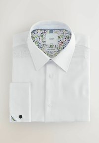 Chemise en coton blanc avec un revers de col intérieur à motifs floraux et des boutons de manchette noirs contrastants. Dotée d'un col classique et d'une fermeture à boutons.