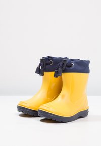 Gele waterdichte rubberen laarzen met een marineblauwe textielboord, ronde neus en rubberen zool met profiel.