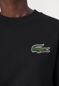 Felpa nera con un logo di coccodrillo verde testurizzato e dettagli rossi, ricamato sulla parte sinistra del petto.