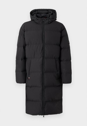 Abrigo acolchado negro con capucha, cierre de cremallera y dos bolsillos laterales. Presenta una textura acolchada y un parche con el logotipo en la manga.