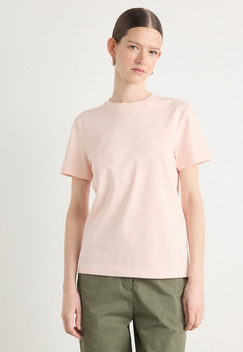 T-shirt in cotone rosa chiaro con maniche corte e scollatura rotonda. Presenta un marchio sottile sul petto. Abbinato a pantaloni verde oliva.