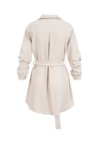 Robe chemise beige à manches longues avec épaules tombantes, pli dans le dos, ceinture à la taille ajustable et poignets à boutons.