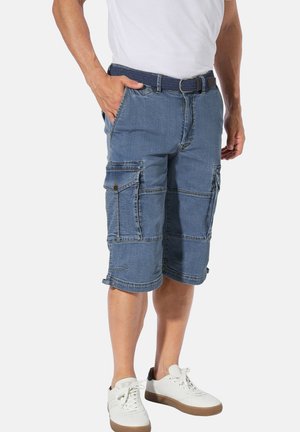 Denim-Cargo-Shorts in Mittelblau mit mehreren Taschen und Umschlagsaum. Getragen mit einem weißen T-Shirt und weißen Turnschuhen. Strukturiertstoff.