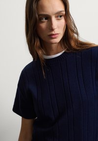 Pull en maille côtelée marine à manches courtes et col rond, présentant une texture verticale et un design uni.