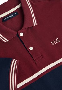 Kastanjefärgad polo-skjorta med vita ränder på kragen och ärmarna, med en knappslå och "POLO KLUBB" broderat i vitt.