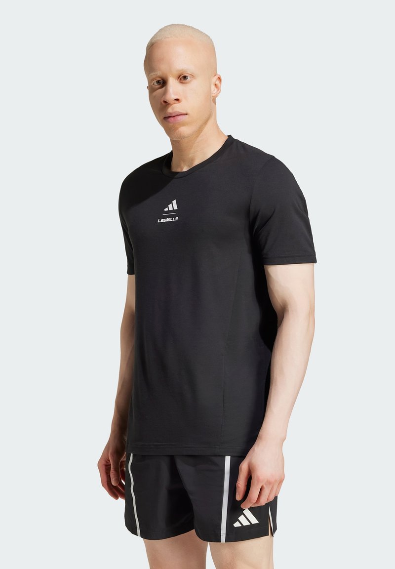 Svart trening T-skjorte med korte ermer, med hvit "LES MILLS" tekst og Adidas-logo på brystet. Glatt, pustende materiale.