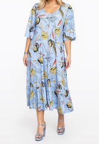 Světle modré květinové šaty s výstřihem do V, krátkými rukávy, vrstveným spodním dílem a živými žlutými a černými rostlinnými vzory. Doplňuje je volán.