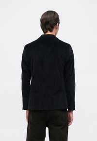 Blazer escuro de bombazina com corte ajustado, ombros definidos e lapelas com entalhe. Apresenta textura subtil e detalhes de design minimalistas.