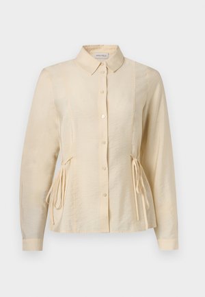 Blouse crème à manches longues avec boutons, col et détails de nouage sur les côtés, légèrement cintrée à la taille.