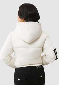 Biała krótka kurtka puchowa z kapturem, z czarnym logo na rękawie i teksturowaną, pikowaną powierzchnią.