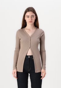 Cardigan beige a costine con maniche lunghe, scollatura a V e bottoni frontali. Abbinato a jeans scuri a vita alta. Design minimalista.