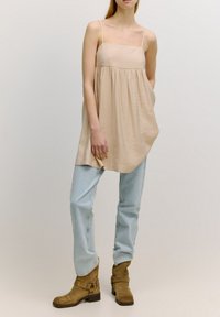 Beige mouwloze tuniek met een gestructureerde afwerking, gecombineerd met lichtblauwe rechte spijkerbroeken en tan enkelboots met gespdetails.