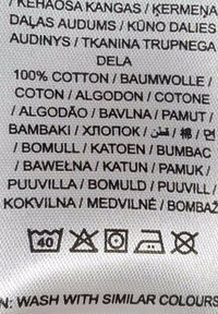 Etiqueta de tela blanca con instrucciones de cuidado e información del material, que indica "100% ALGODÓN" en varios idiomas, con símbolos de lavado.