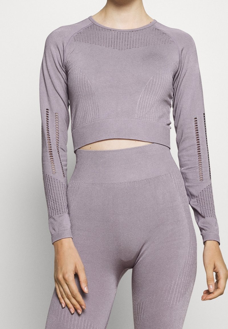 Světlofialový krátký top s dlouhými rukávy, žebrovaným vzorem a výřezem v pase. Rukávy mají síťované panely pro lepší prodyšnost.
