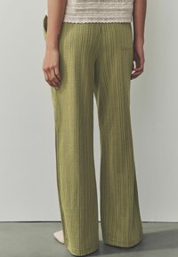 Pantalons larges à motifs verts avec des rayures verticales et une texture douce, dotés d'une poche arrière et d'une coupe décontractée.
