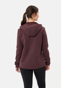 Bordeaux hoodie met een trekkoordkap, gladde textuur, lange mouwen en een licht afgeronde zoom. Gemaakt in combinatie met zwarte leggings.
