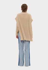 Beżowy sweter dzianinowy z odkrytymi plecami, w oversize'owym kroju i prążkowanej fakturze, w zestawieniu z jasnoniebieskimi spodniami o szerokich nogawkach z bocznymi paskami.