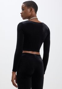 Top cropped in velluto nero a maniche lunghe con scollatura rotonda, caratterizzato da una texture liscia e una silhouette aderente.