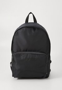 Mochila preta de nylon com formato arredondado, com um bolso frontal com fecho e logótipo em relevo. Inclui alças ajustáveis e pega superior.
