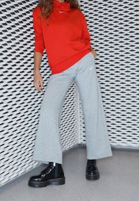 Röd huvtröja med en liten Nike-logotyp, ihopparad med grå utsvängda sweatpants med en Nike-logotyp. Skorna är svarta lackskinnboots.