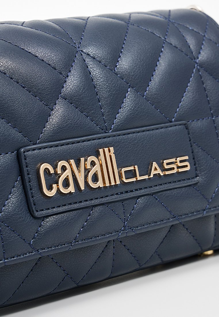 Bolso de cuero acolchado azul marino con una placa de logo en tono dorado. Diseño compacto con patrón de diamantes y detalle de costura en contraste.