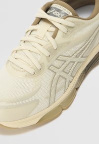 Beige spordijalanõud, millel on tekstureeritud võrkkangas ja stiilsed elementid ning mustriga tallad. Paelad on samas värvitoonis.