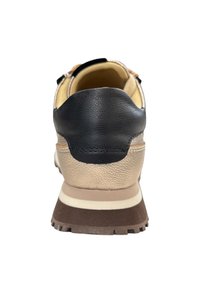 Sneaker met een beige en zwart leren bovenwerk, gewatteerde kraag, bruine rubberen zool en een gestructureerd detail aan de achterkant met witte strepen.